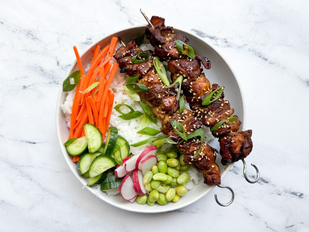 air fryer hoisin chicken thighs atop rice bowl with fresh vegetables